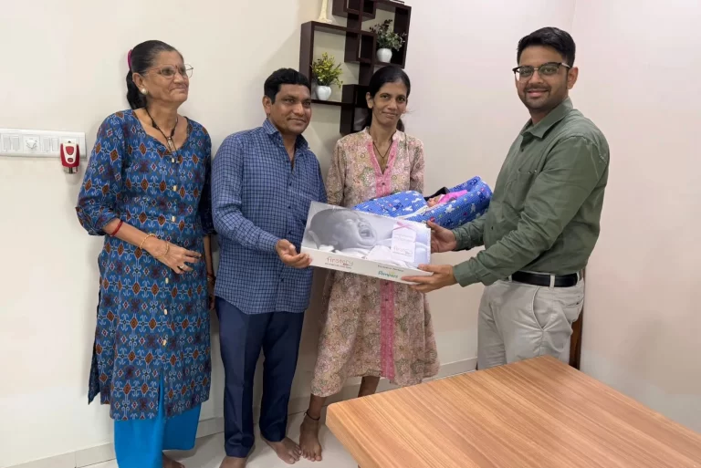Four people posing with a baby gift set in a room